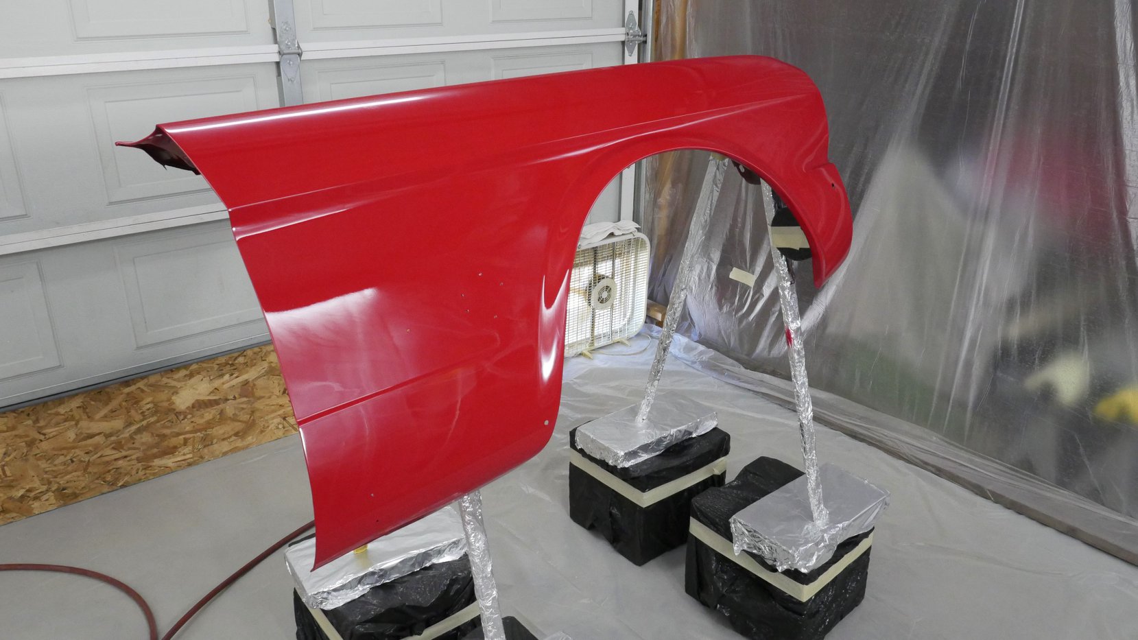 A fender with a fresh application of clear coat. A temporary paint booth and creative stand help make it possible.